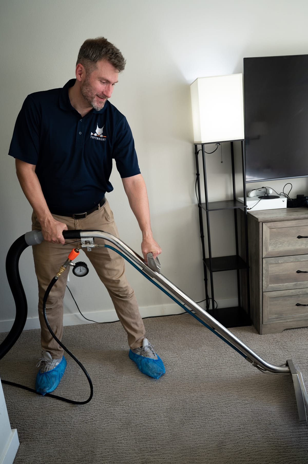 Kevin guiding a carpet cleaning wand in a room while wearing blue shoe covers